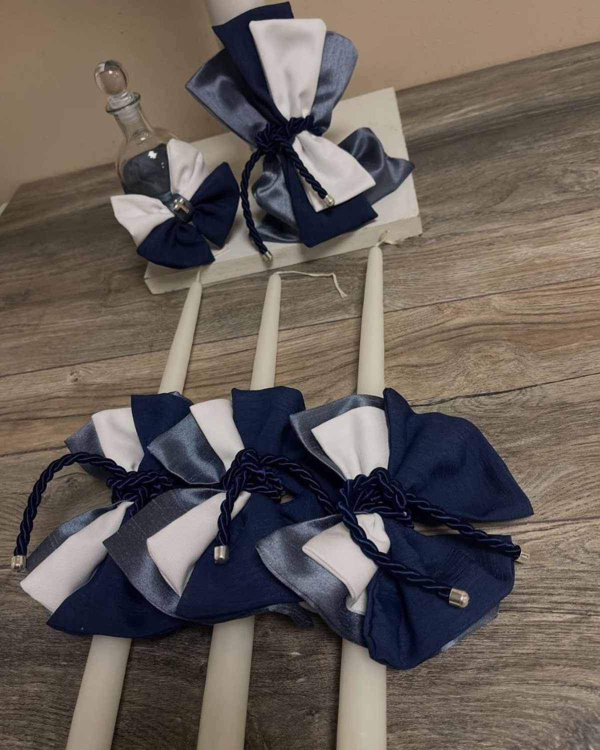 White taper candles adorned with navy blue and white fabric bows on wood.
