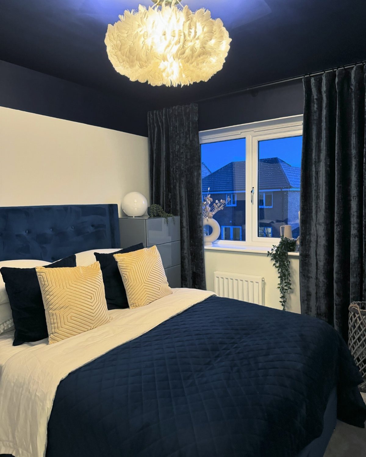 Navy velvet curtains framing a window in a bedroom with navy blue bedding.