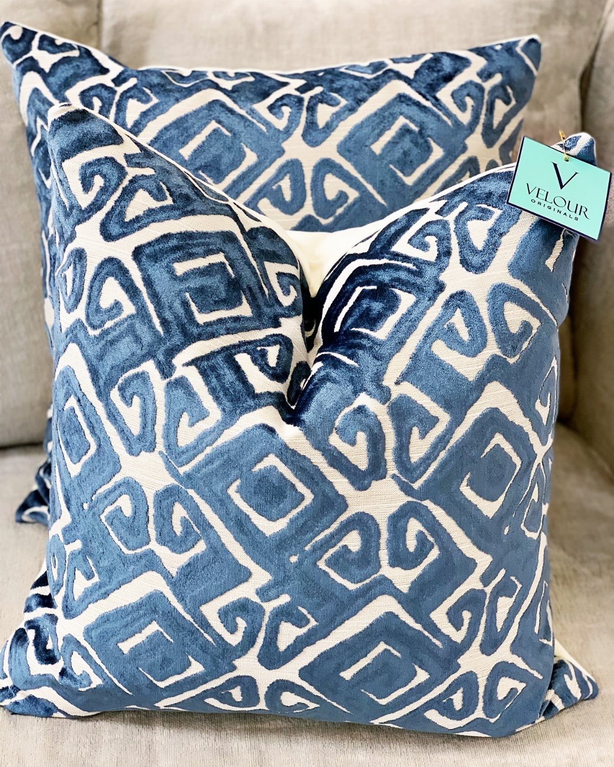 Navy blue and white patterned velvet pillows resting on a light grey sofa.