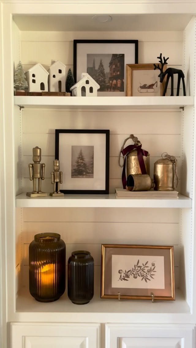White built-in shelves decorated with neutral Christmas ornaments, framed art, and lit candles.