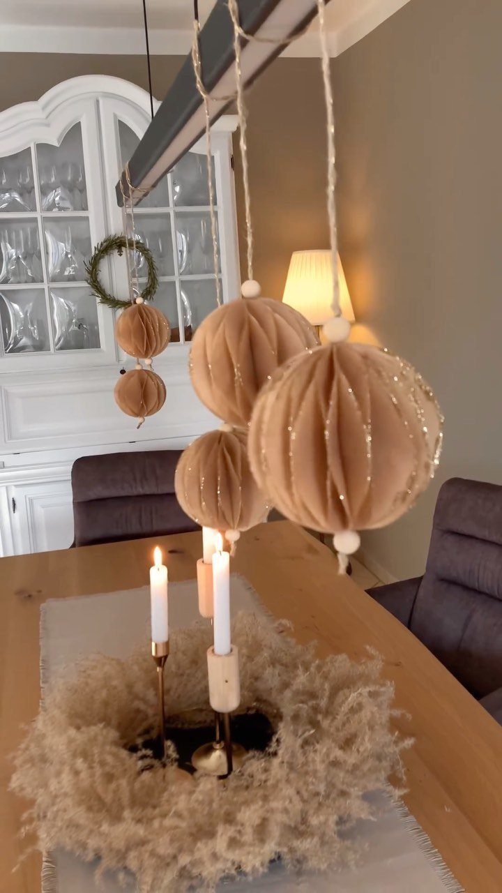 Beige fabric sphere ornaments hanging over a dining table with neutral Christmas decor.