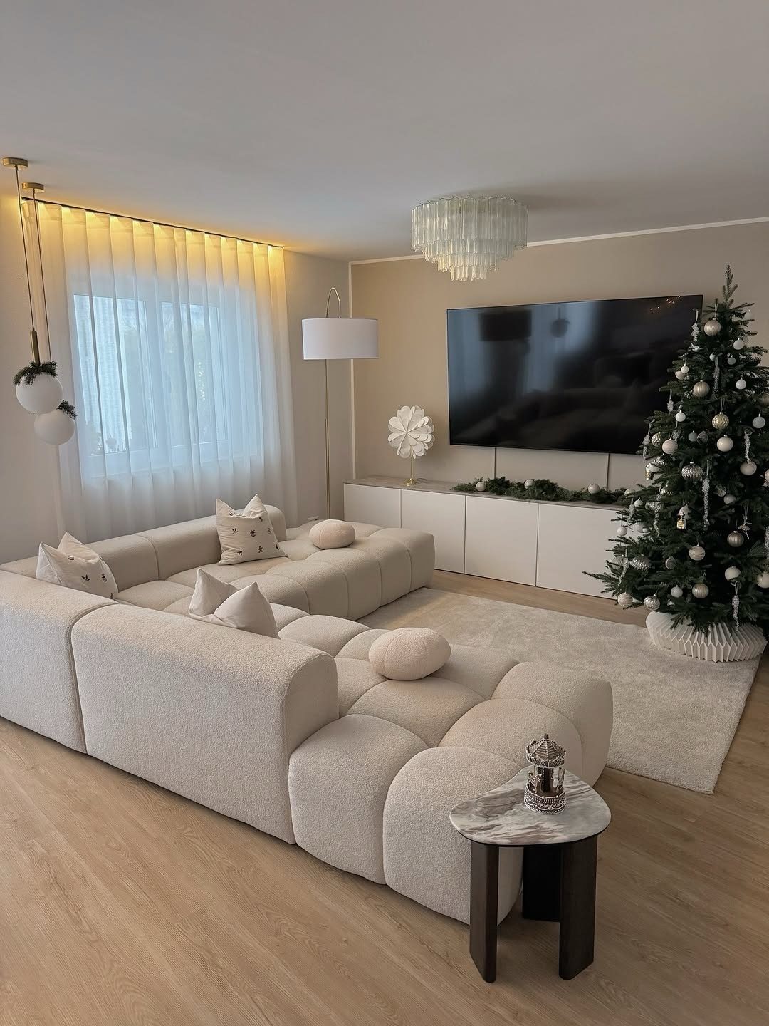 Modern living room with cream furniture and a minimally decorated white Christmas tree.