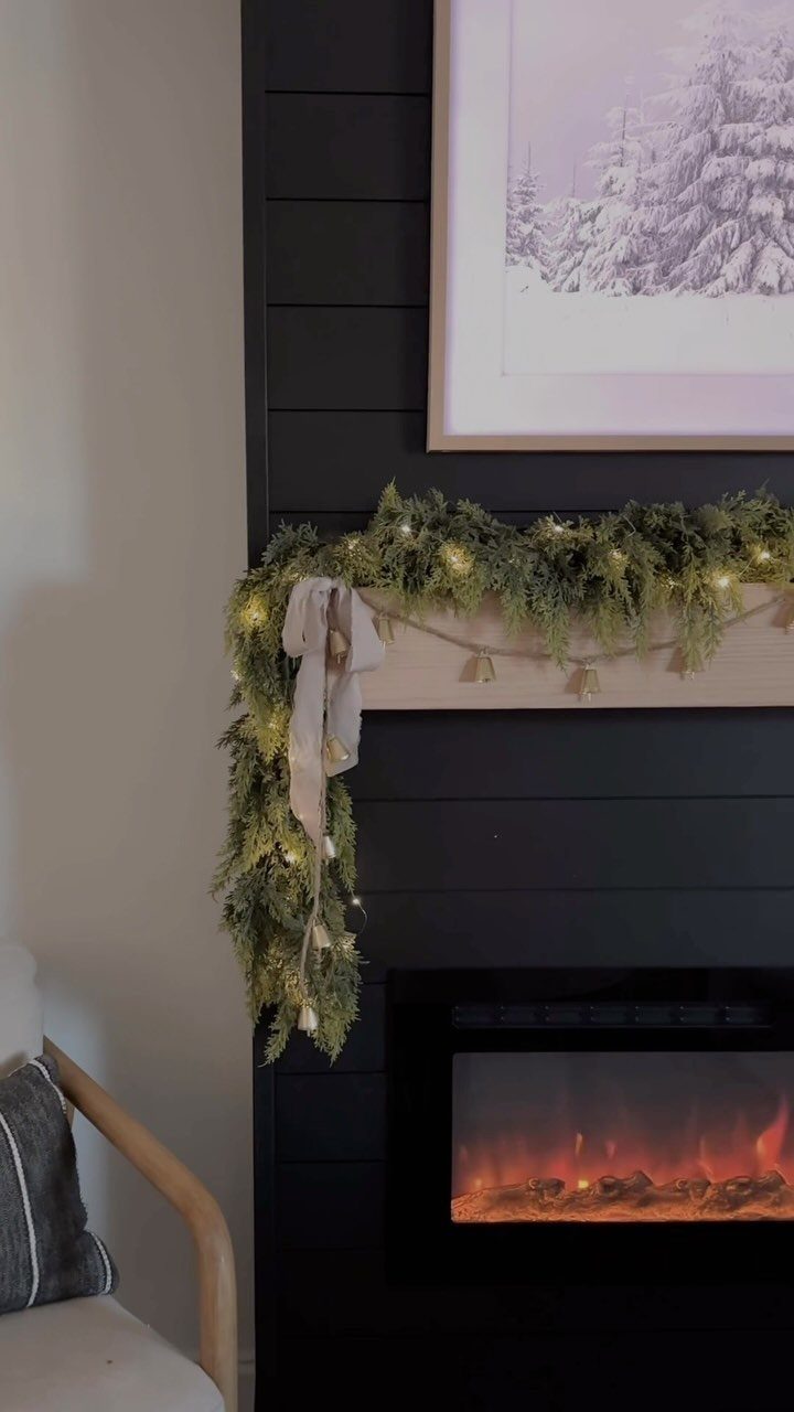 Green pine garland with lights and a neutral bow on a fireplace mantel