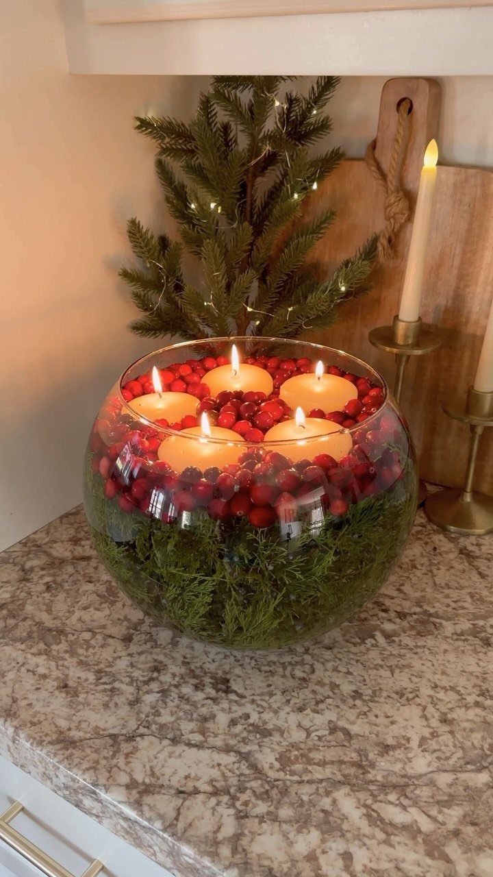 Glass bowl filled with green pine needles and red cranberries with floating candles.