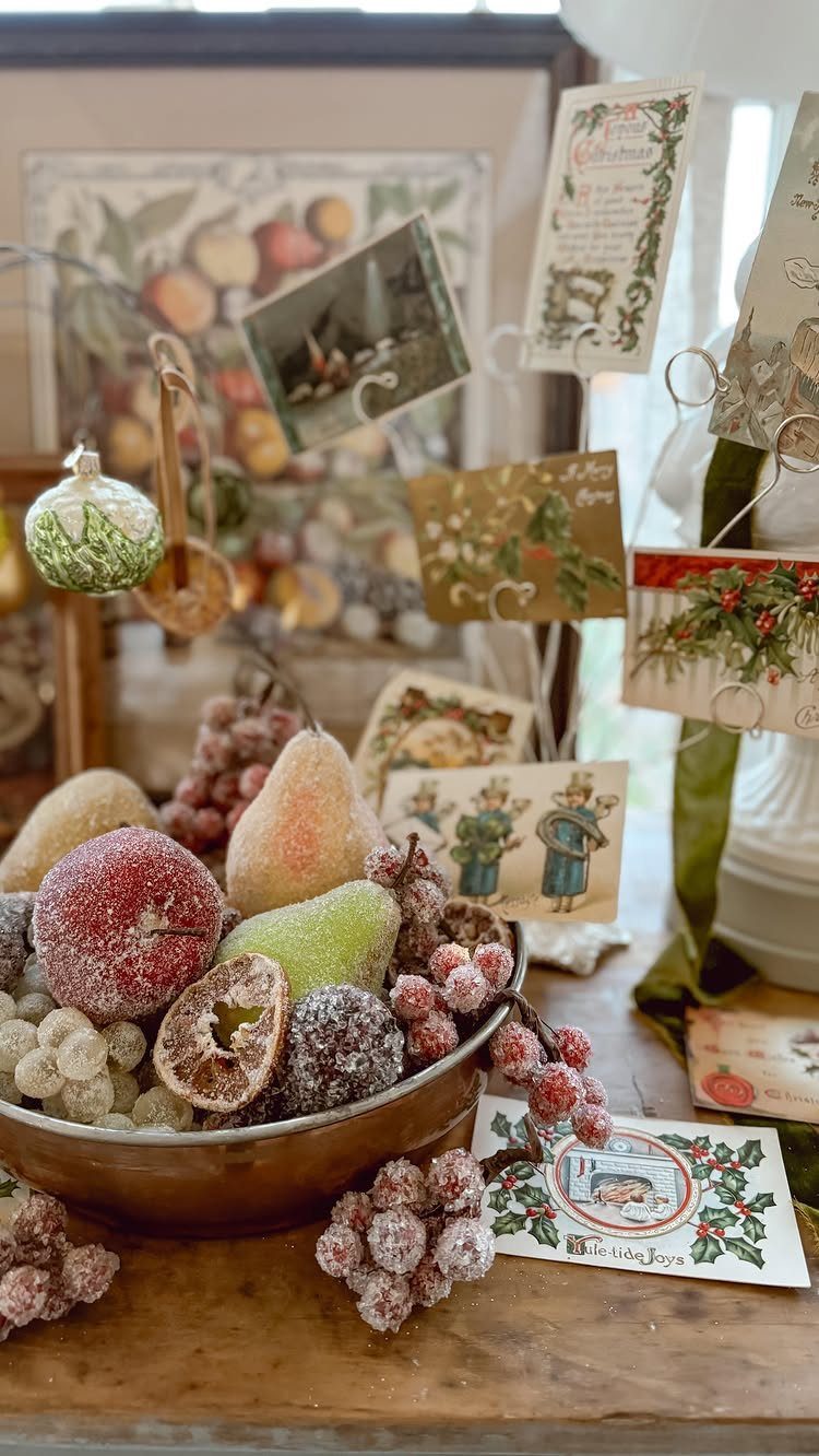 Frosted artificial fruits in a metal bowl with vintage Christmas postcards behind.