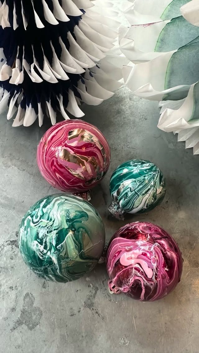 Marbled pink and teal Christmas ornaments on a grey stone surface with paper decorations.