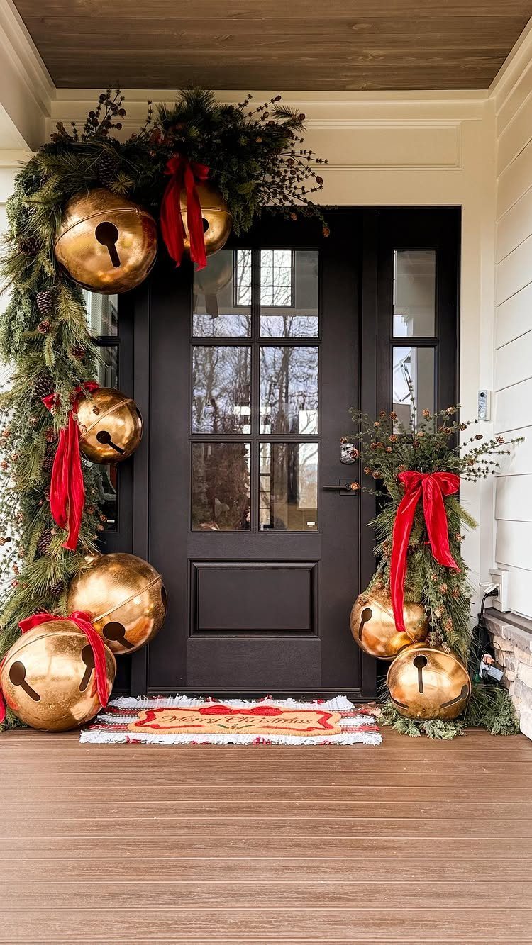 Black front door adorned with evergreen garland, large gold bells, and red ribbons.