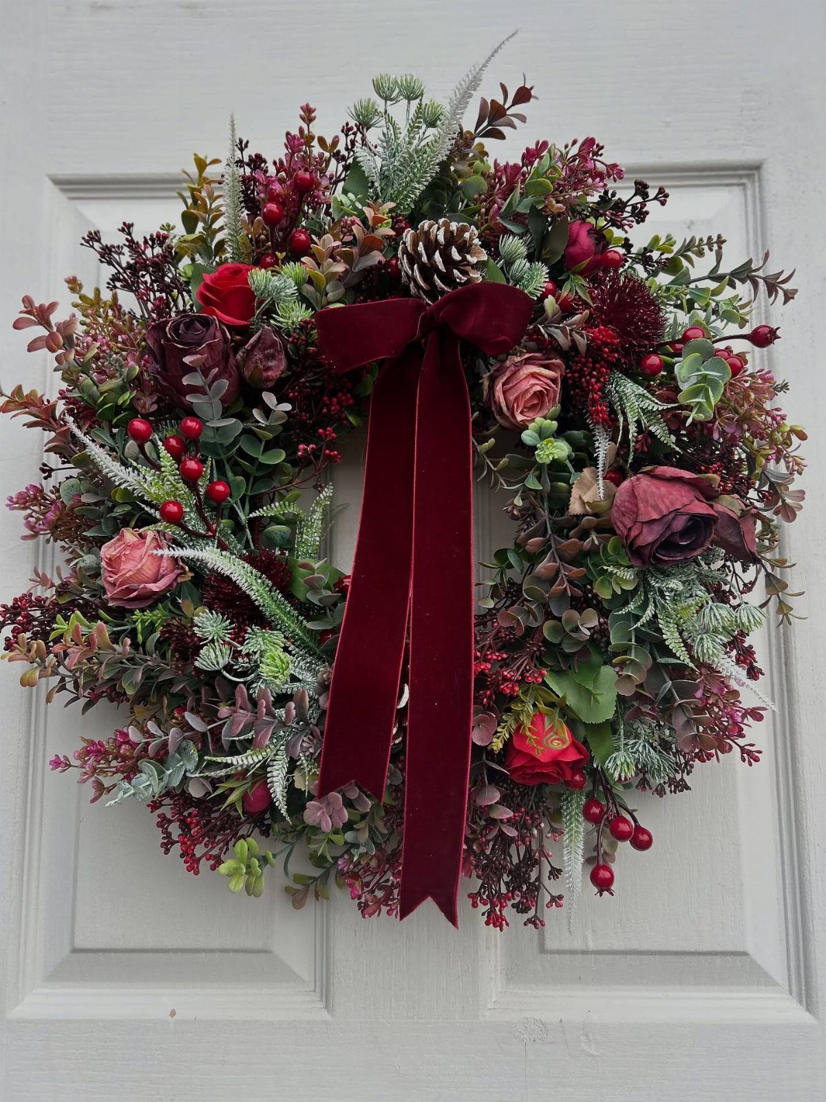 Christmas wreath with red roses and burgundy bow hanging on a white door