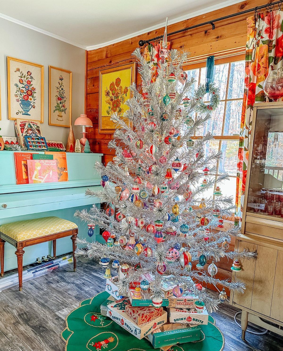 Silver tinsel Christmas tree with colorful ornaments in a cozy wood-paneled room.
