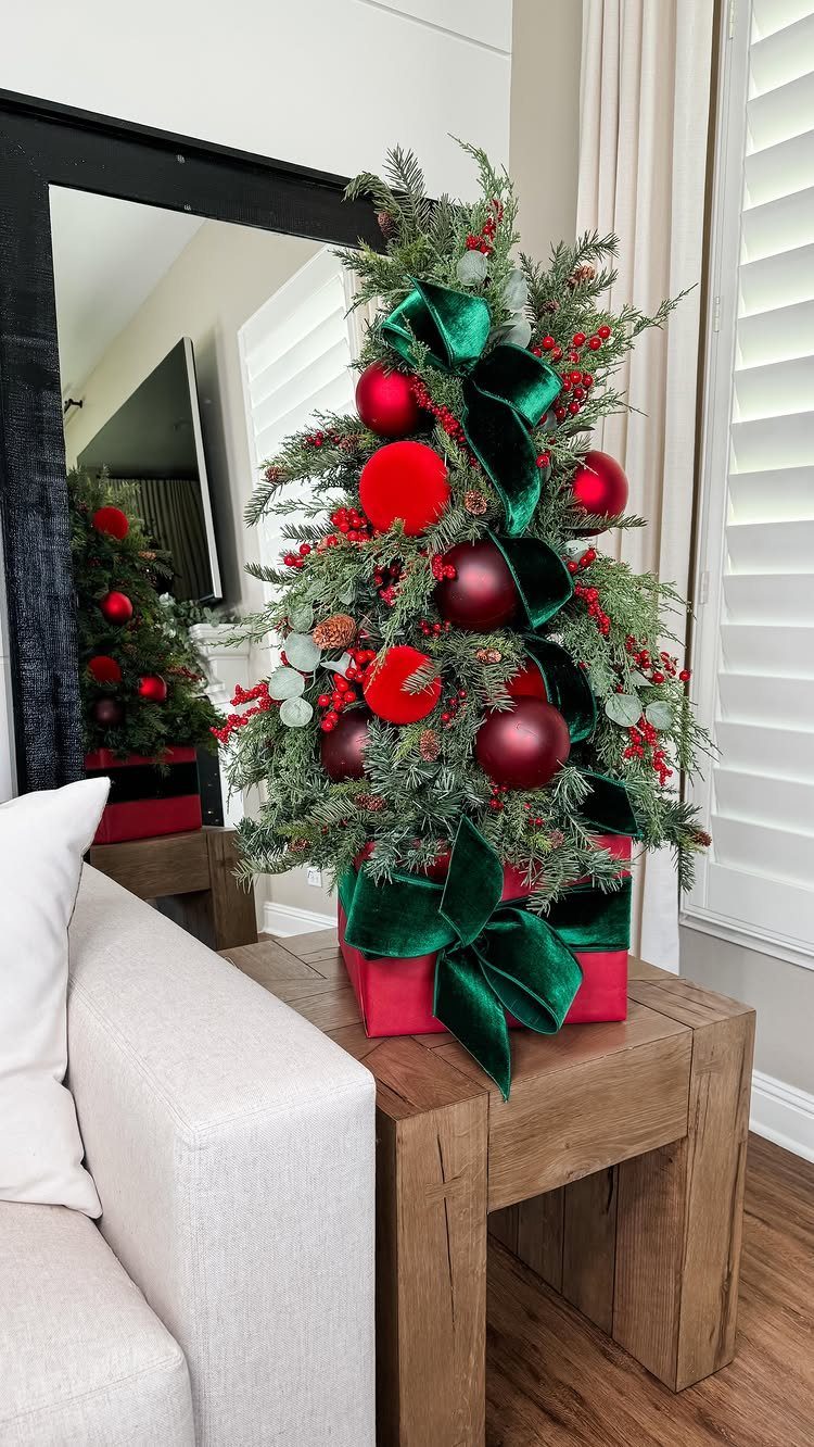 Small decorated Christmas tree on a red gift box atop a wooden table.