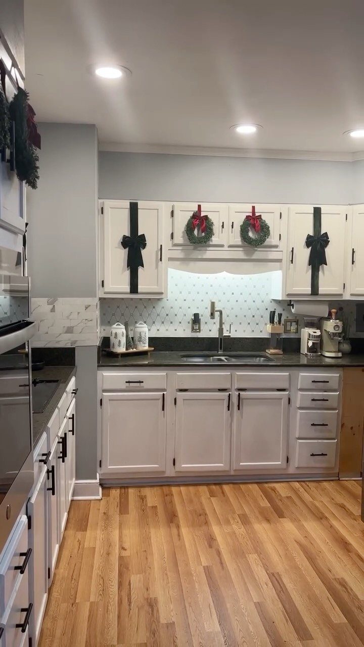 White kitchen cabinets decorated with black vertical bows and small Christmas wreaths.