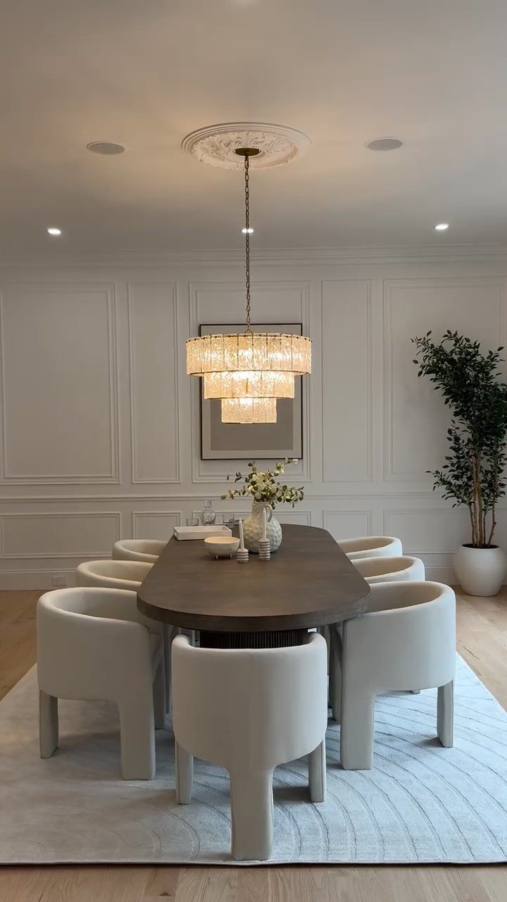 Dark oval dining table with curved white chairs under a tiered gold chandelier.