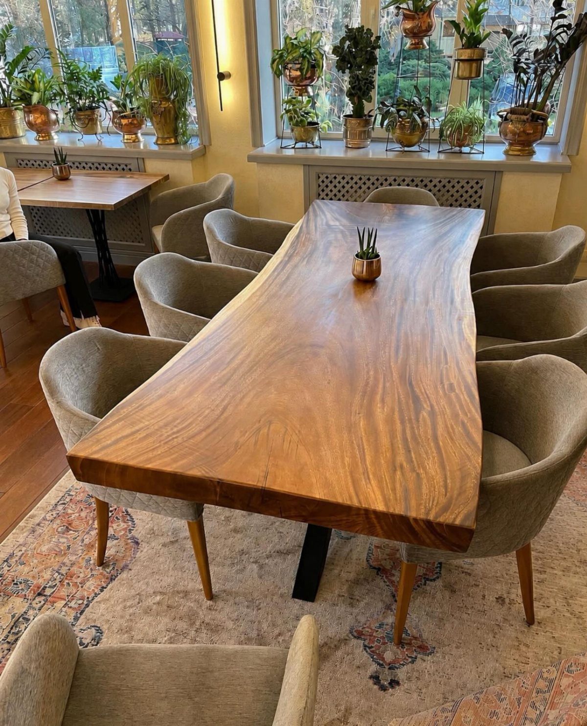 Live-edge natural wood dining table surrounded by grey chairs in a sunlit room.