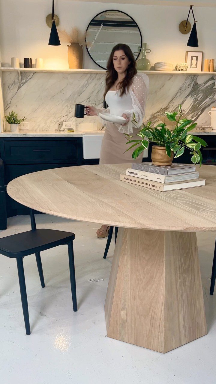 Round wooden pedestal dining table with a potted plant and books in a kitchen.