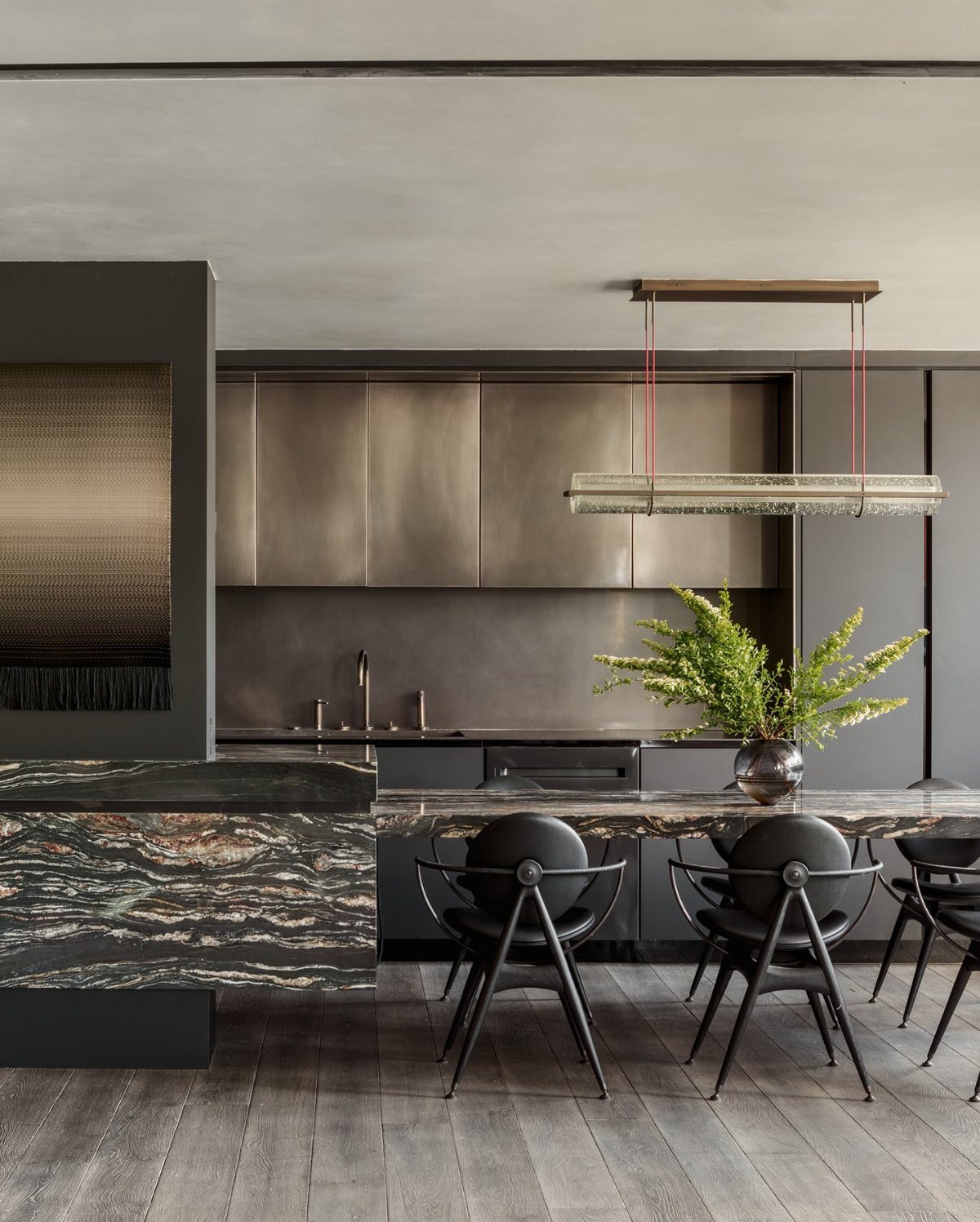 Modern dining area with marbled island, black sculptural chairs, and metallic kitchen cabinets.