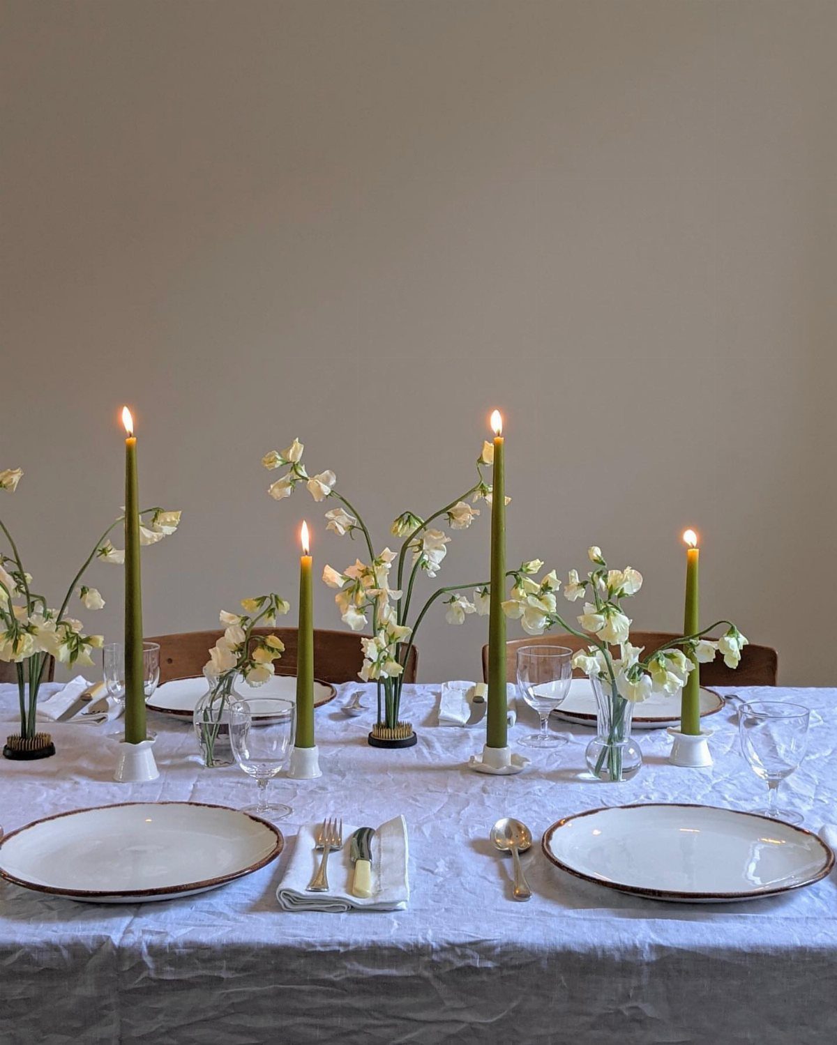 Simple white plates and clear glassware on a linen tablecloth with green candles.