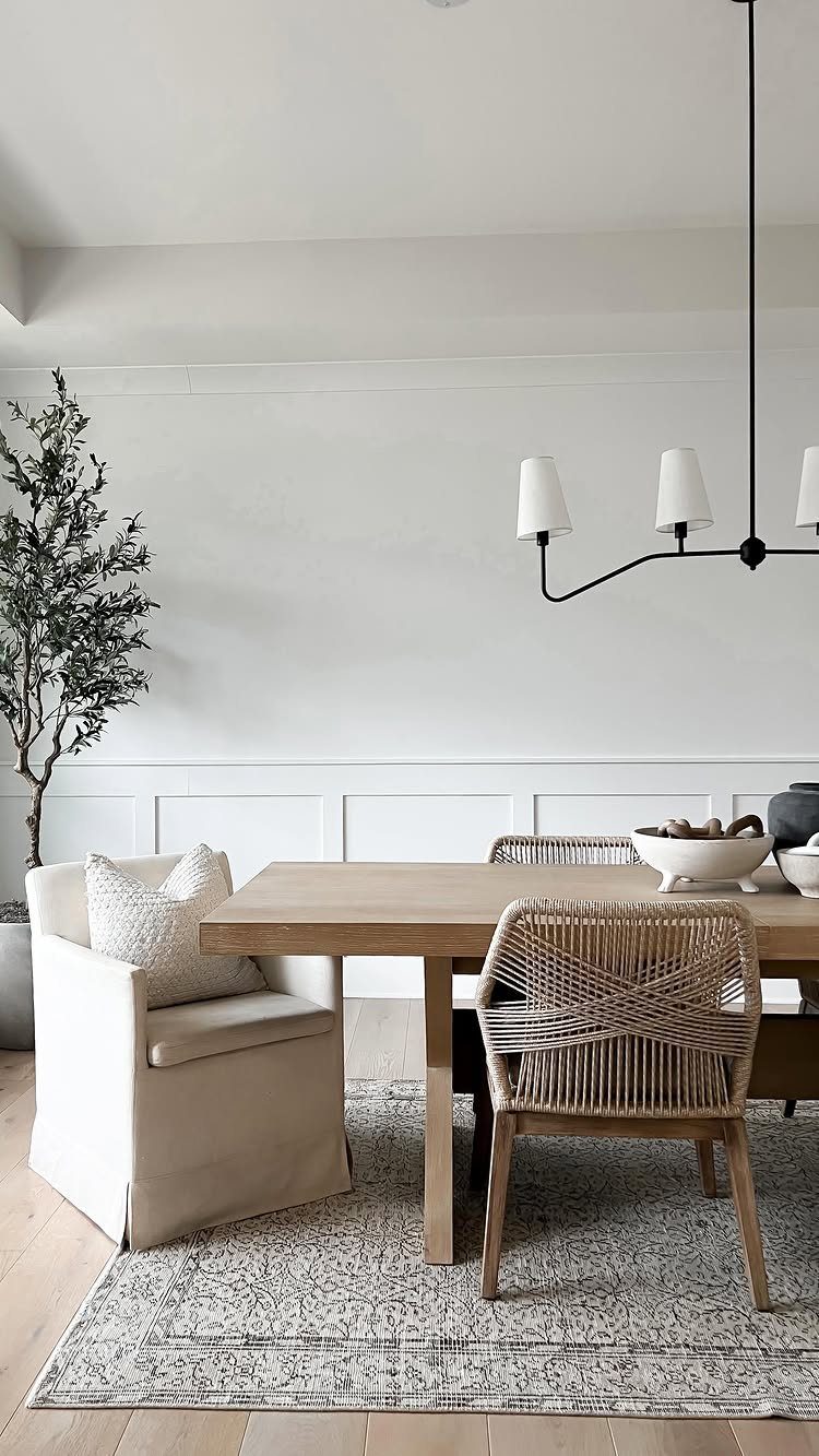 Light wood dining table with woven and upholstered chairs in a bright modern room.