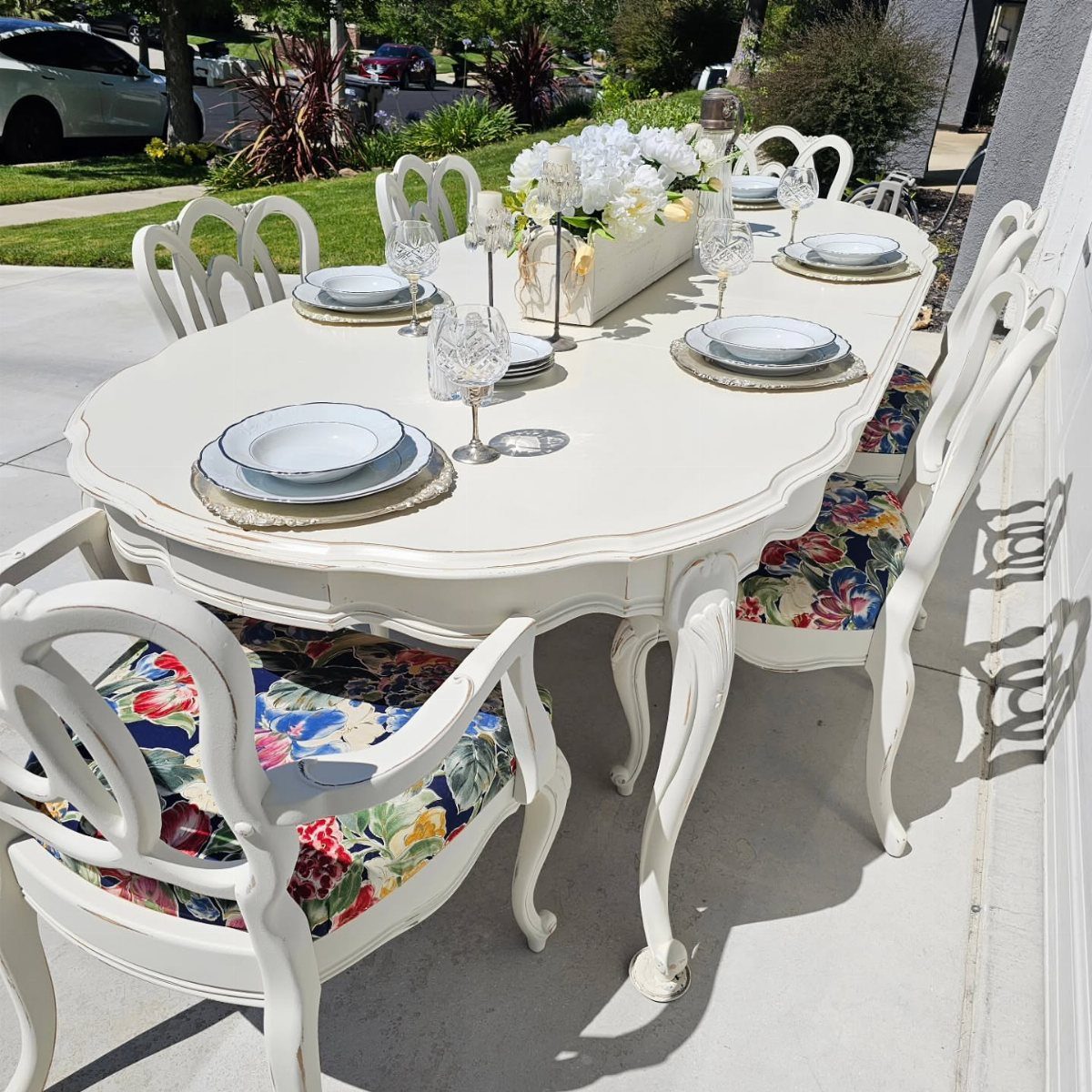 White painted dining table with distressed edges and floral upholstered chairs on patio