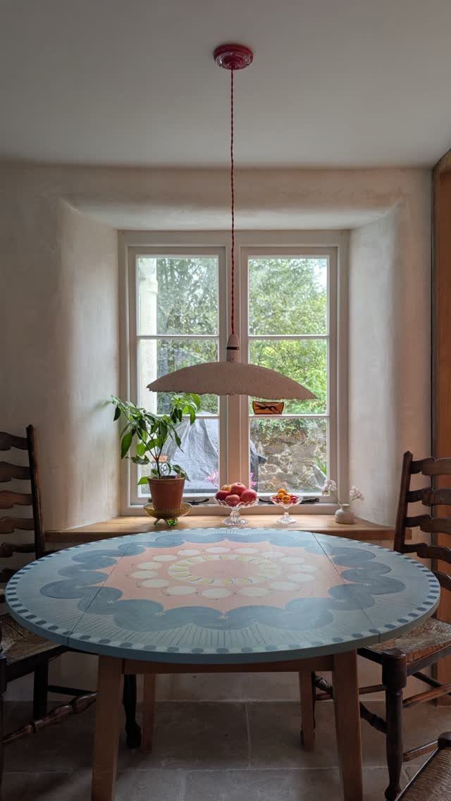 Round wooden dining table with a blue and pink painted mandala design on top.