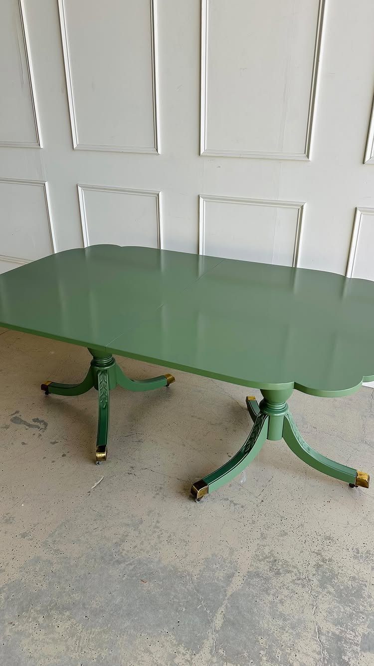 Sage green painted dining table with glossy finish against a white paneled wall.