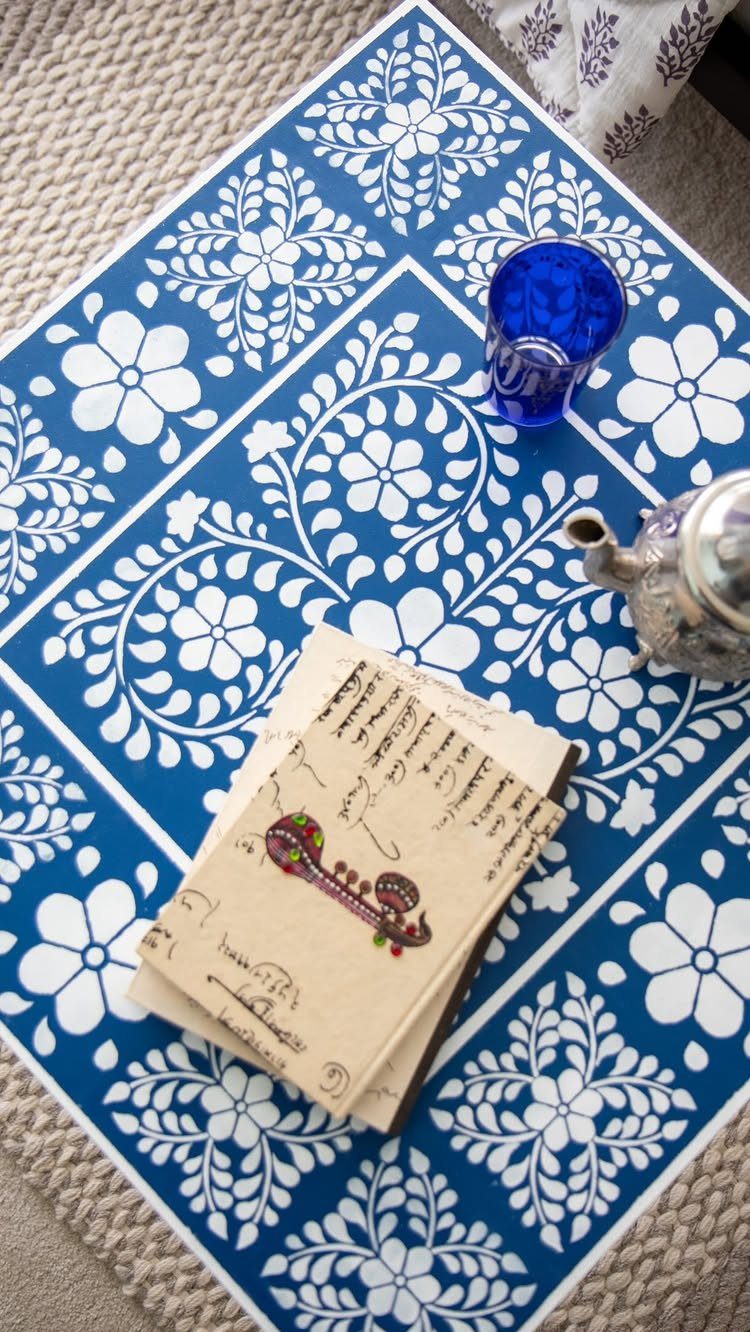 Blue table with white stenciled floral patterns holding a teapot and notebooks.