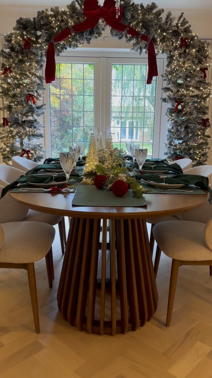 Round wooden dining table with green runner and red accents under a festive arch.