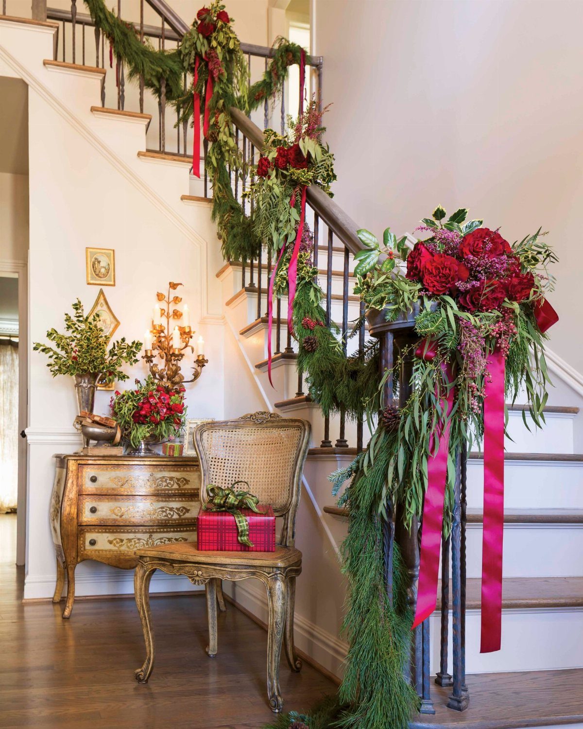 Staircase decorated with green garlands, red ribbons, and red flowers against white walls.