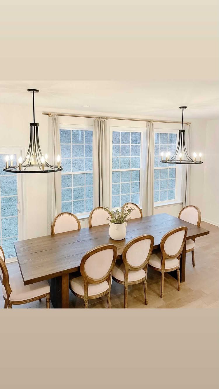 Two black wagon-wheel chandeliers hanging over a dark wood dining table and chairs.