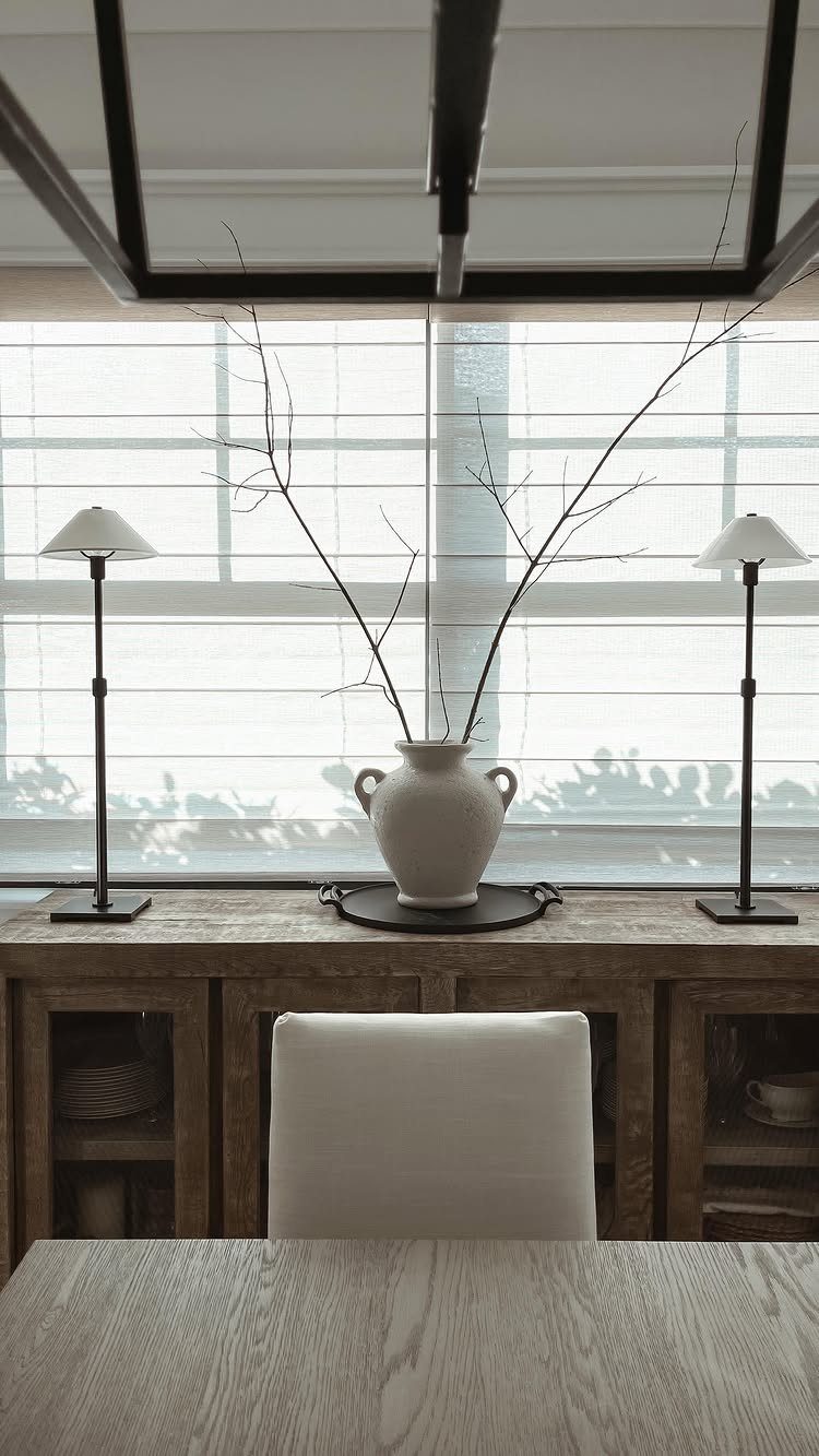 Rustic wooden sideboard with white vase and black lamps in neutral dining room