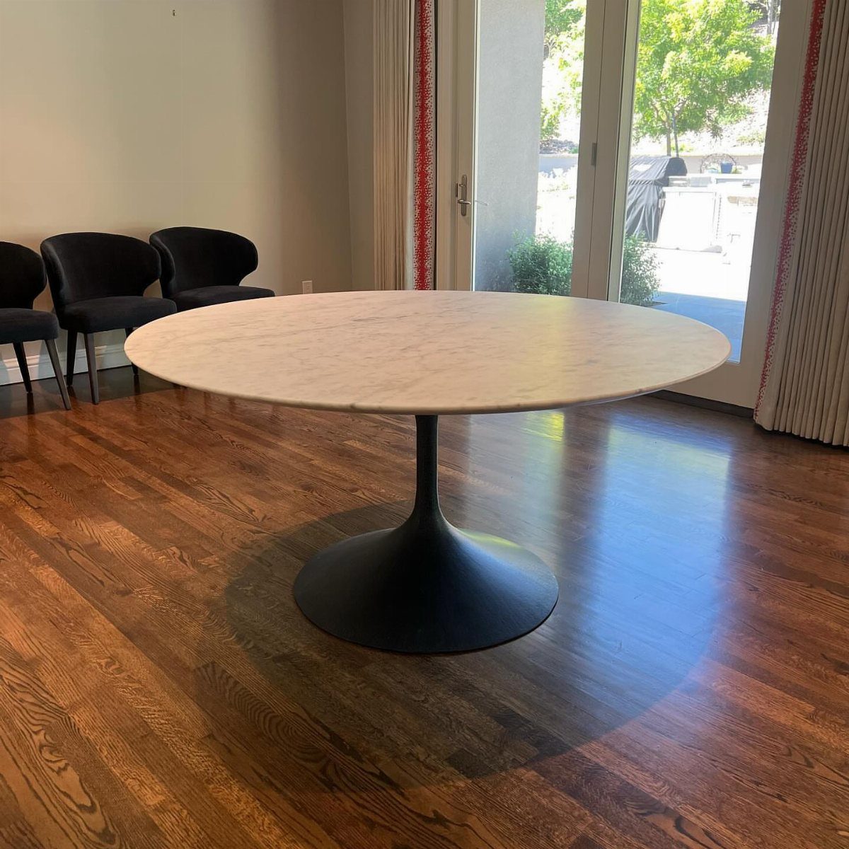 Round white marble dining table with black pedestal base on dark wood flooring