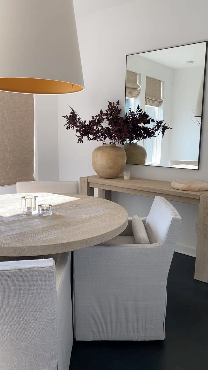 White upholstered slipcovered dining chairs around a round light wood table.