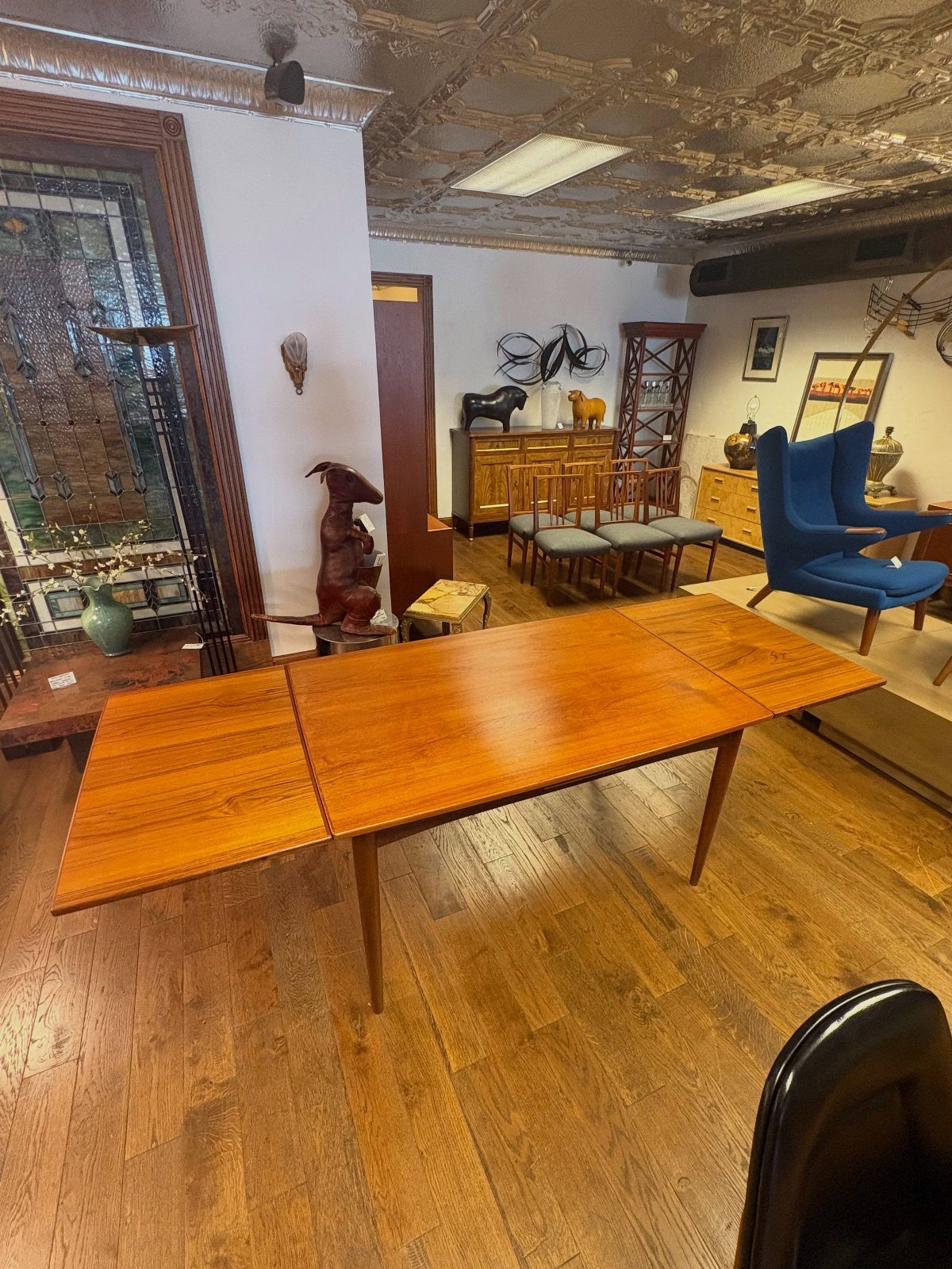 Rectangular wooden dining table with extension leaves partially open in a furniture showroom.