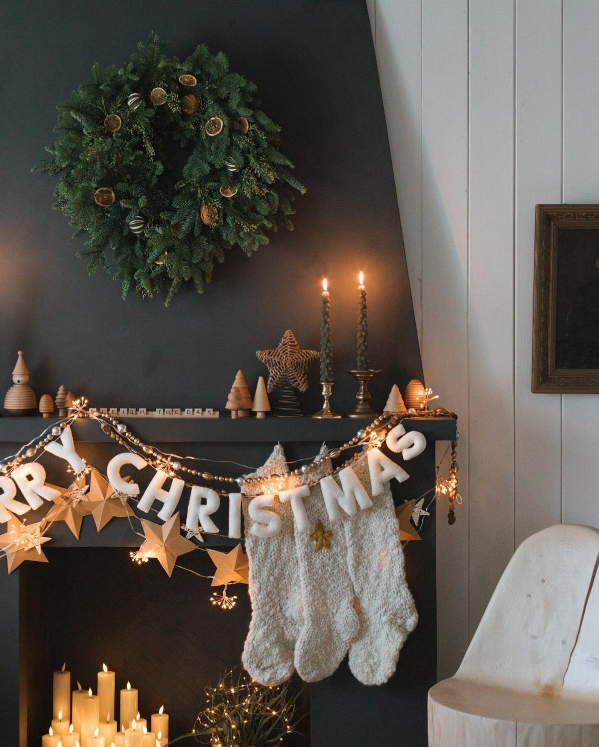 Christmas mantel decor with a green wreath, white stockings, and Merry Christmas banner.