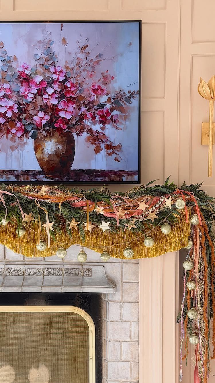 Fireplace mantel decorated with green garland, gold fringe, and pink and orange ribbons.