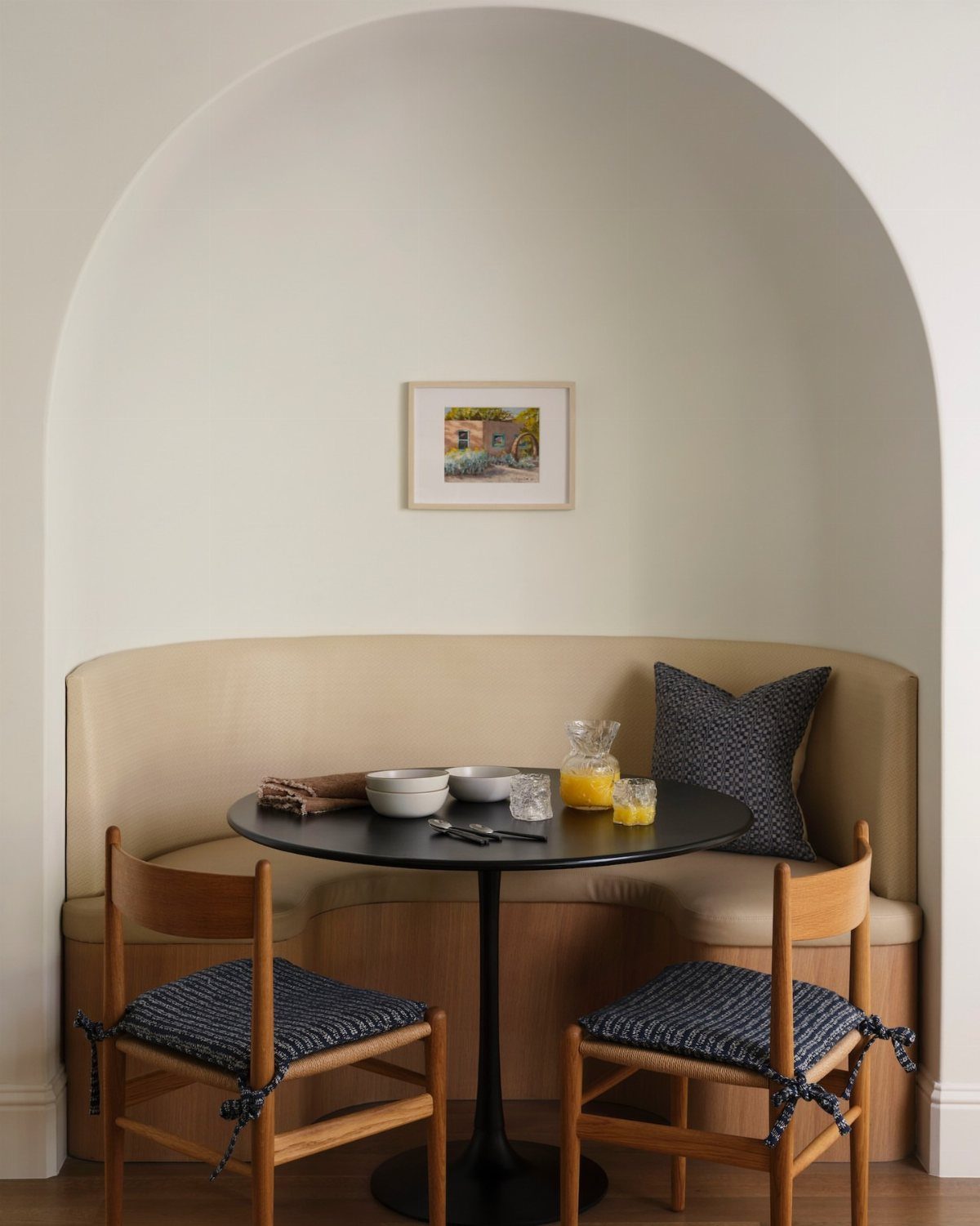 Small breakfast nook with a curved beige banquette and round black table in alcove