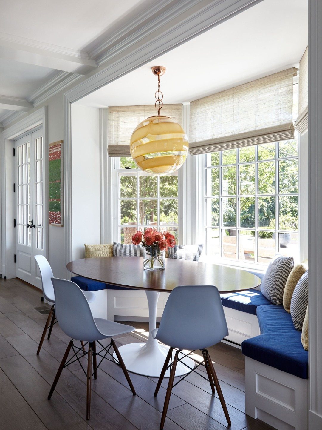 Breakfast nook with oval table and blue banquette seating inside a bright bay window