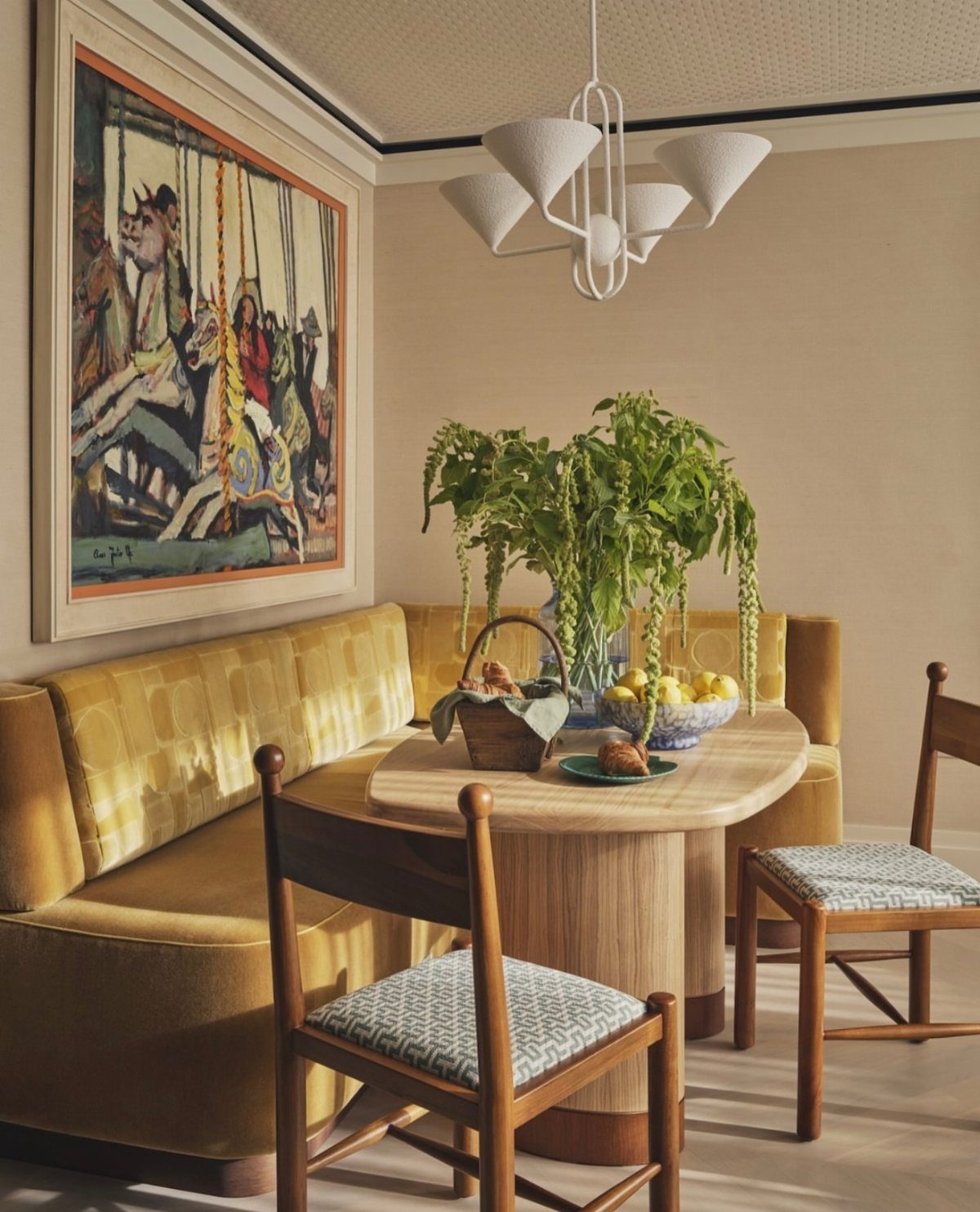 Small breakfast nook with yellow velvet banquette, oval wooden table, and modern lighting.