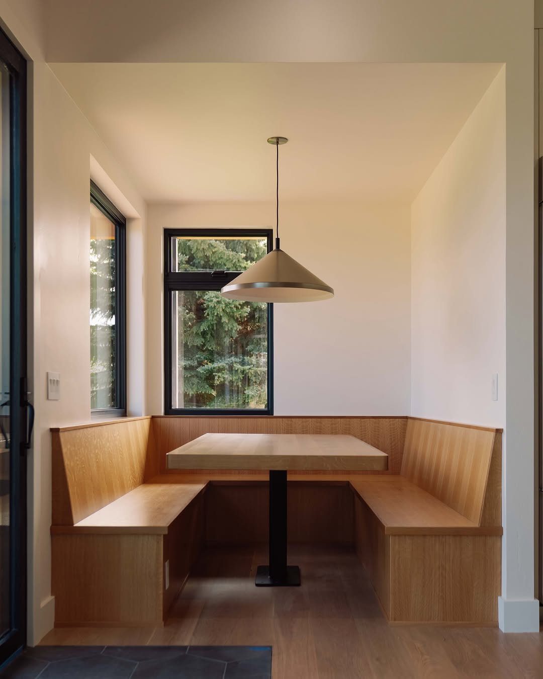 Wooden L-shaped banquet seating and square table in a bright small breakfast nook.