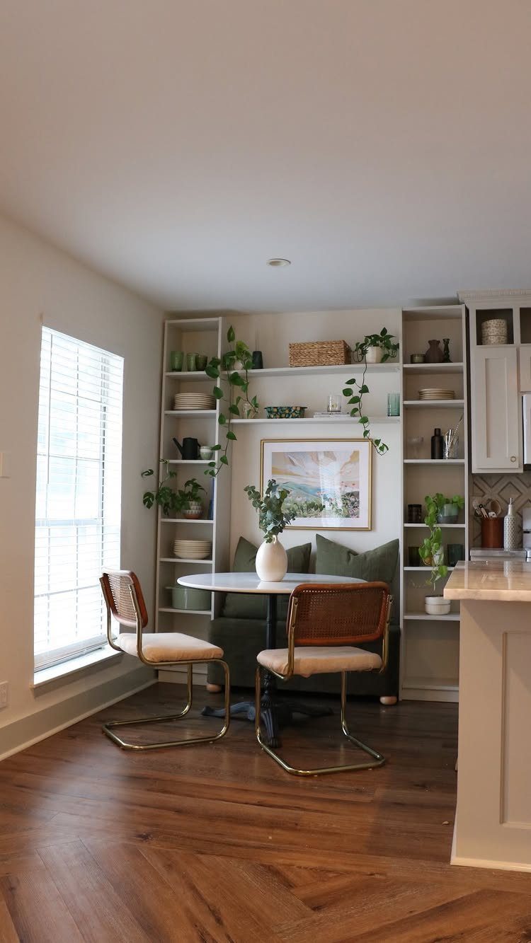 Round white table and green banquette surrounded by white built-in open shelving units.