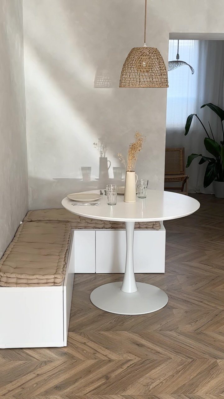 Round white dining table with L-shaped built-in bench seating and woven pendant light.