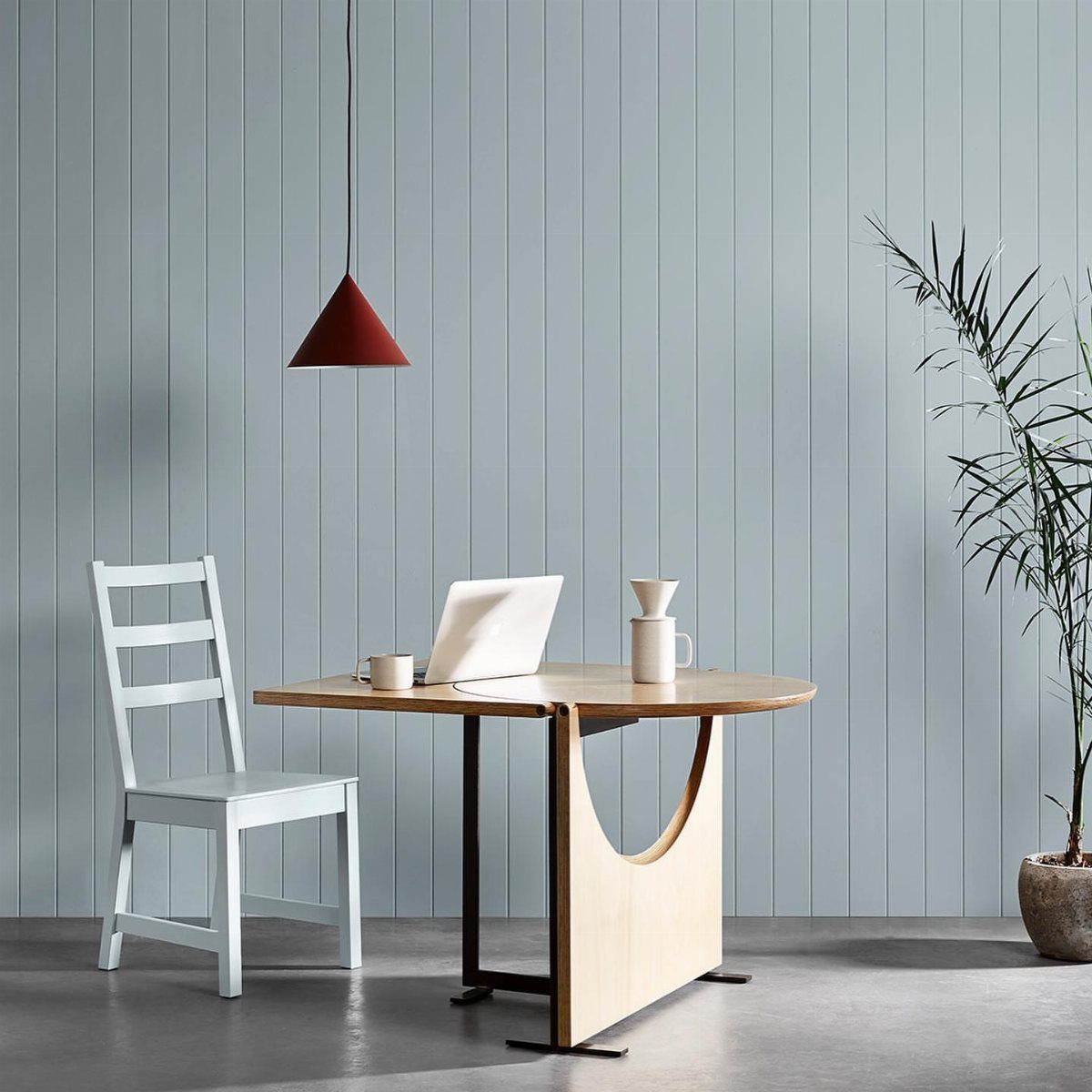 Small light-wood dining table and white chair against a blue paneled wall.