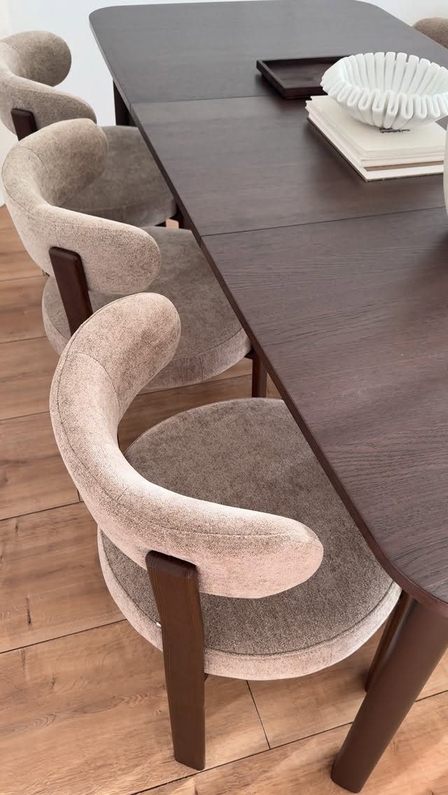 Dark wood dining table with curved beige upholstered chairs on light wood flooring