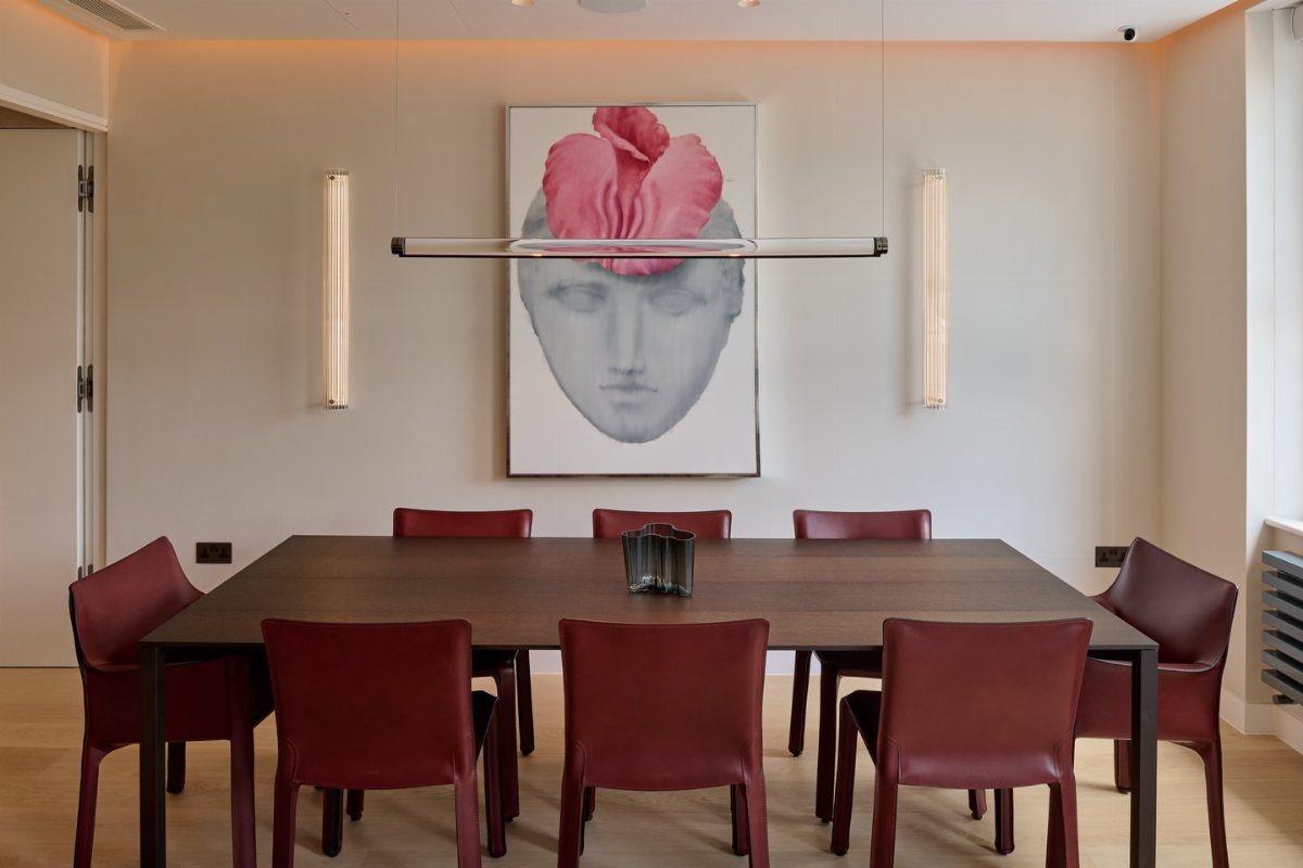 Dark wood dining table with red leather chairs and large face artwork.