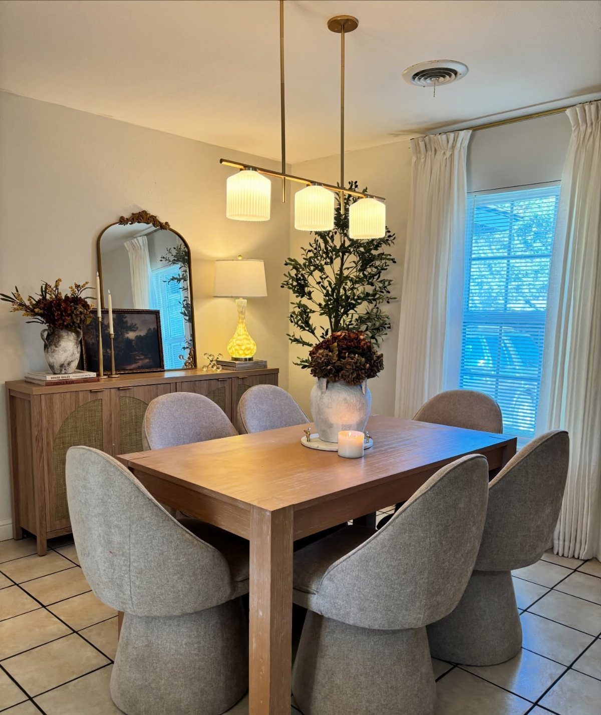 Wooden dining table with grey chairs, gold pendant lighting, and an arched mirror.