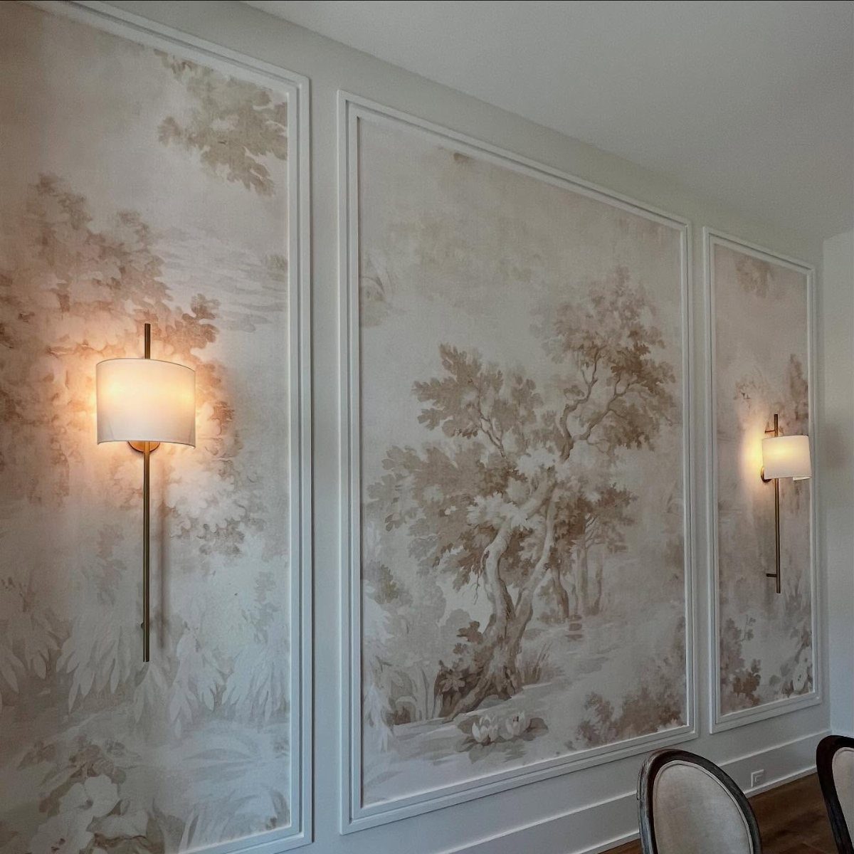 Scenic landscape wallpaper panels on a wall with two warm glowing wall sconces.