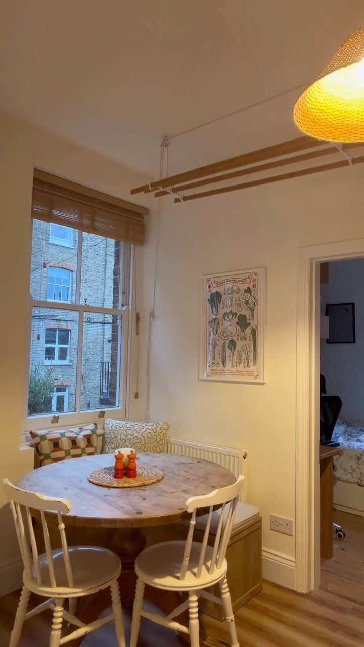 Round wooden dining table with white chairs and built-in bench seating by a window.