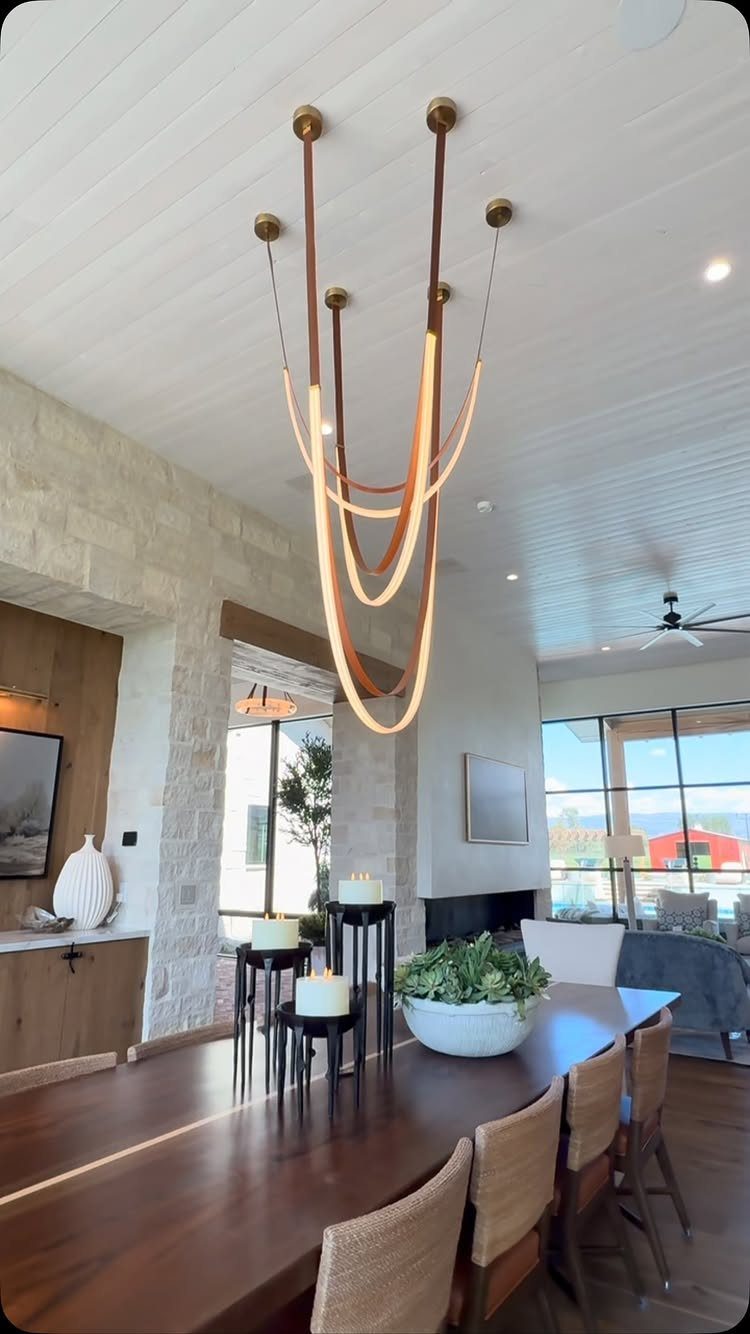 Sculptural curved gold light fixture hanging over a long wooden dining table.