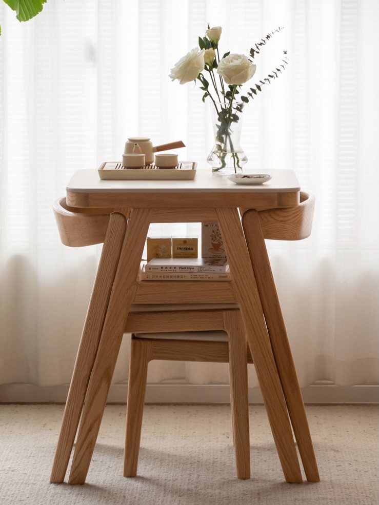 Small wooden dining table with a tea set and white roses in a vase.