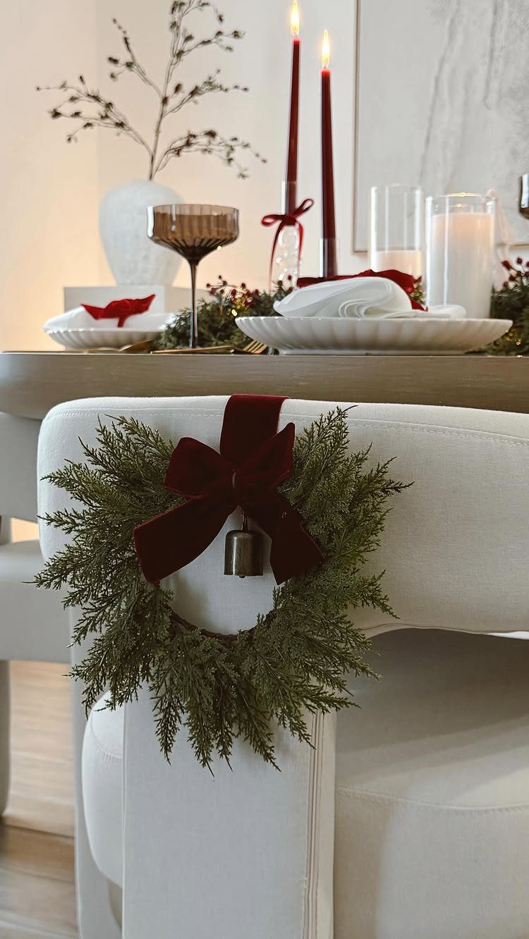 Green evergreen wreath with red bow on a white chair by a Christmas table