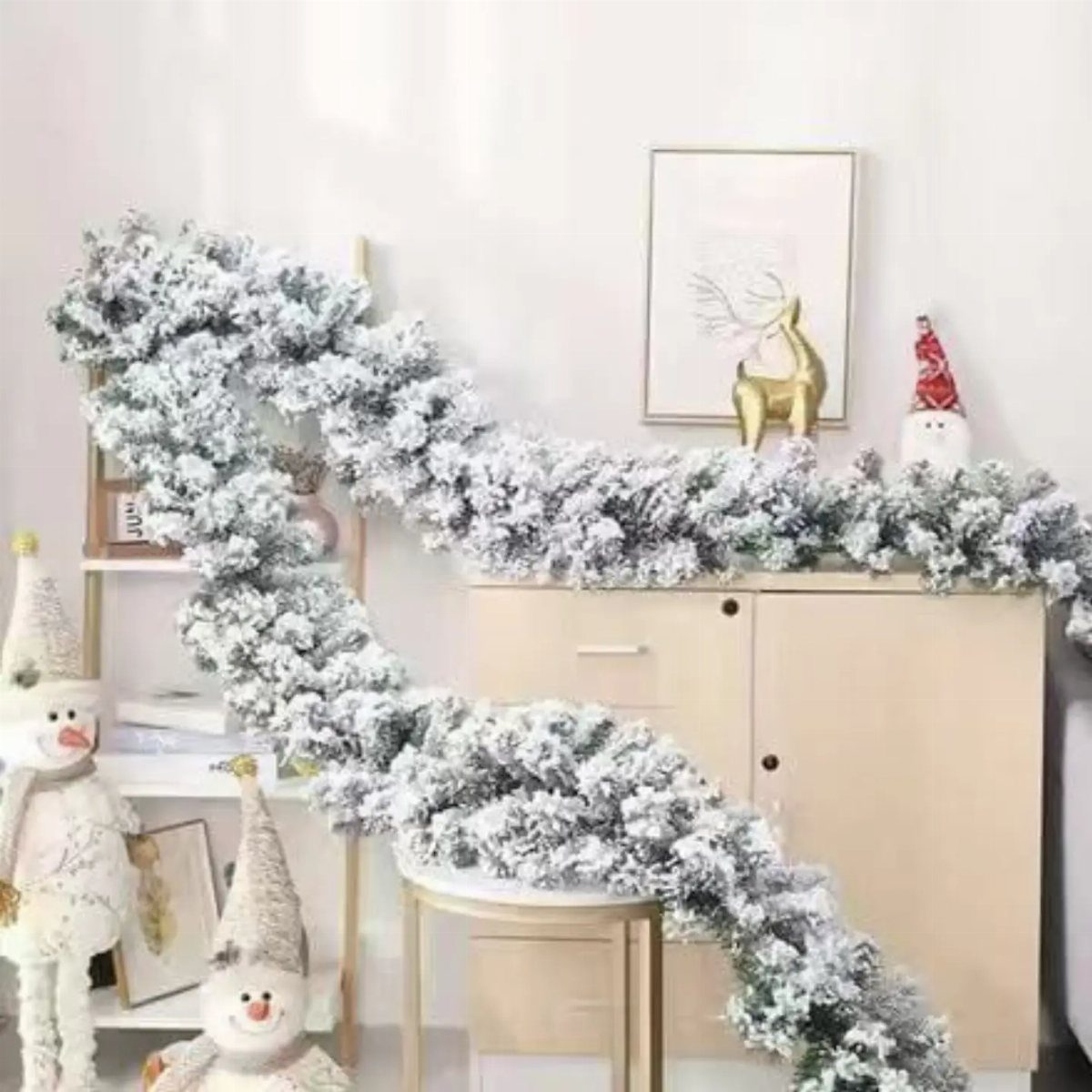 Flocked white Christmas garland draped over a light wood cabinet and shelving unit.